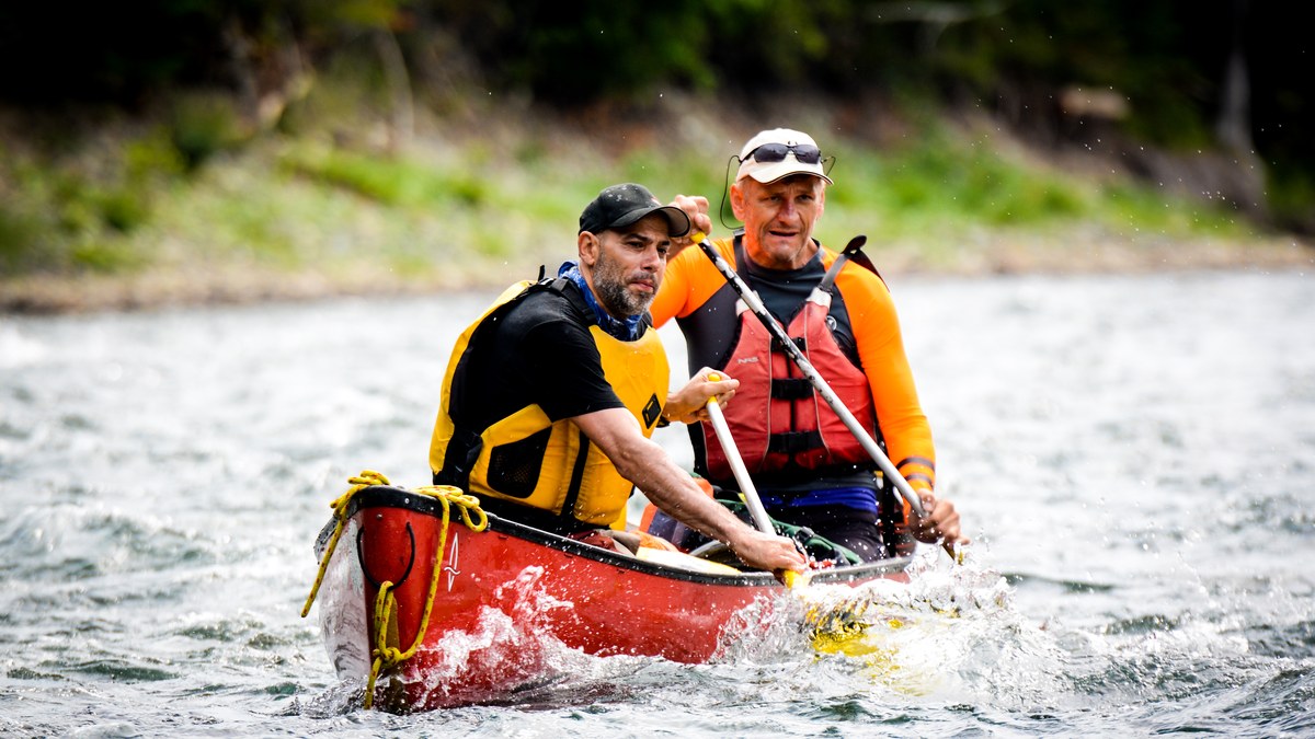 Deux pagayeurs en gilets de flottabilité jaunes dans un canoë rouge sur une rivière vive