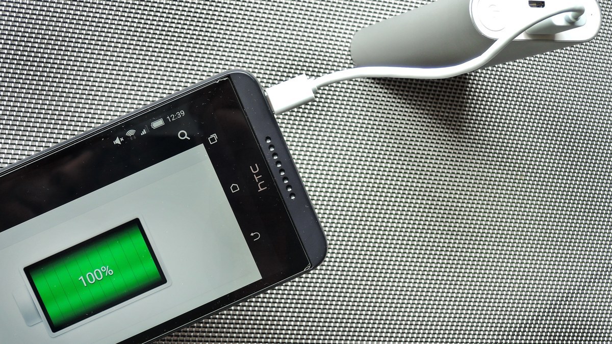 Randonneur vérifiant une batterie externe avec un téléphone sur un sentier